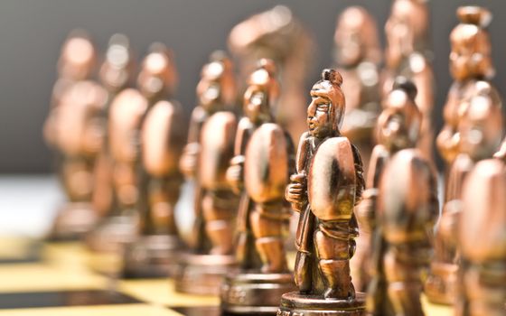 Brass chess piece in focus with other blurred pieces image in background