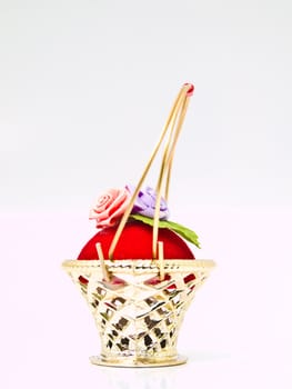 A miniature metalic wicker decorated by roses on a red velvet isolated on white background