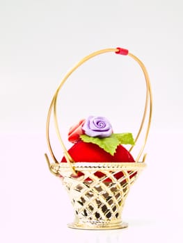 A miniature metalic wicker decorated by roses on a red velvet isolated on white background