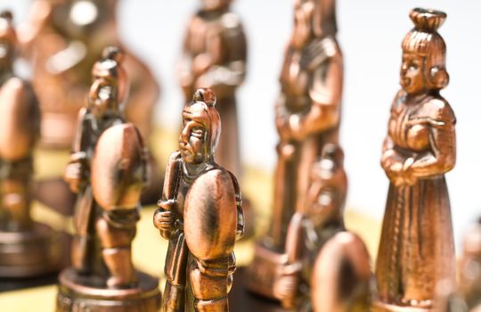 close up of a pawn and queen brass chess piece on a checkerboard with white background