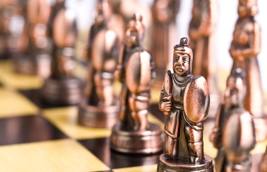 Brass chess piece in focus with other blurred pieces image in background