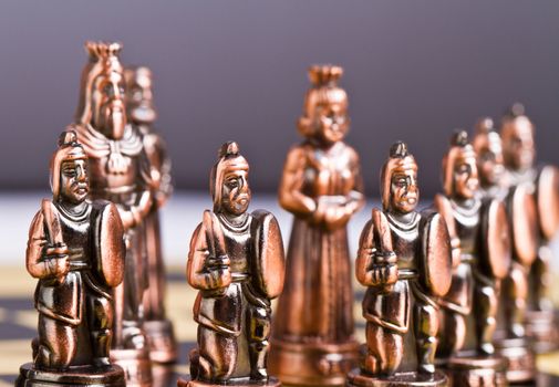 pawn pieces arrenged in front of the king and queen of a brass chess set