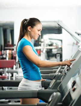 attractive young woman adjusts the treadmill at the beginning of training, do fitness in the sport club