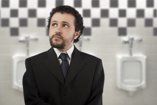 businessman with a distracted look urinating in urinals