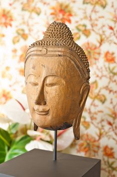 Buddha head in front of floral wallpaper