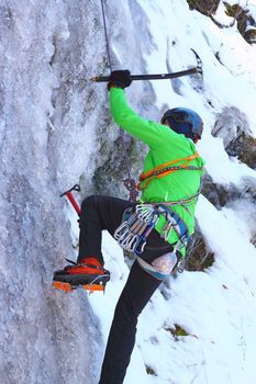 man in green jacket climbing an ice wall - motion blur on ice ax
