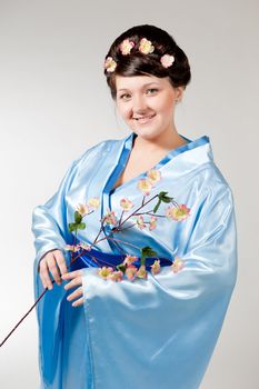 Woman in blue kimono with a branch of cherry blossoms .