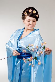 Woman in blue kimono with a branch of cherry blossoms .