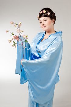 Woman in blue kimono with a branch of cherry blossoms .