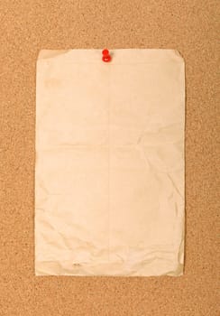 Wrinkled brown envelope attached to cork board with red pin. Empty space for your design.