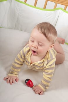 Baby yawns in his bed with toy on the hand