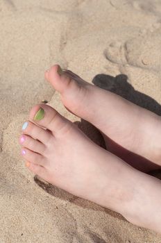 Baby foots with multicolored pedicure on the sand