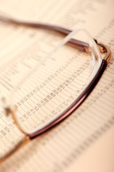 Macro of financial data through eyeglasses, laying on newspaper.