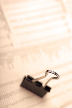 Macro of black paperclip against financial newspaper, warm filter.