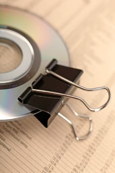 Close photo of paperclip attached to disk laying on financial newspaper.