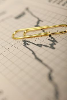 Macro of growing stock market trend graph in financial newspaper and golden paperclip above.