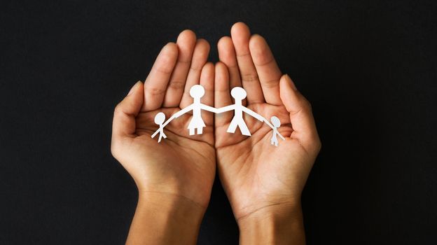 Hands holding a cut out paper family. 