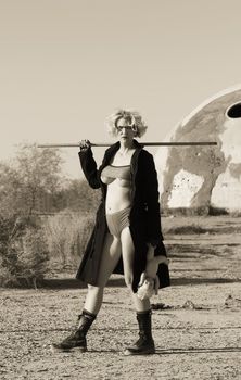 Female science fiction model close up in a desolate location posing with a doll and a wooden stick.