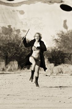 Female science fiction model in a desolate location attacking with a wooden stick.