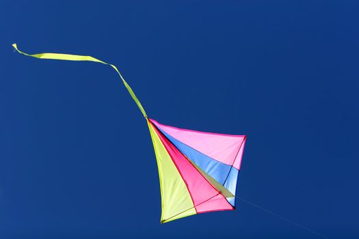 a kite flying against a blue sky in sunlight, bright colors and streaming tail