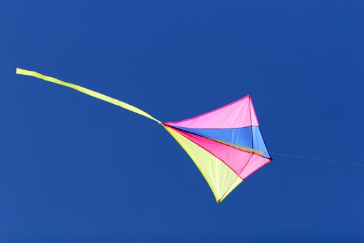 a kite flying against a blue sky in sunlight, bright colors and streaming tail