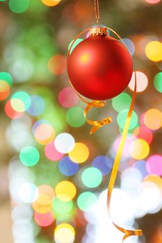 Red frosted Christmas ornament with colorful lights in background.