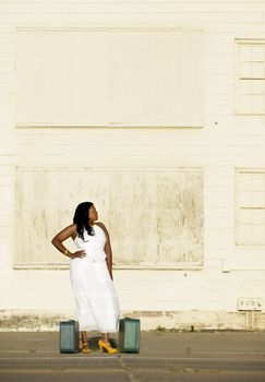 African American woman with suitcases waits outside an industrial building.