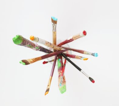 Paintbrushes in a glass jar against a white background, shot from above.