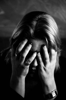 Close up of blonde woman in a studio setting hiding her face in her hands.