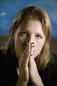 Portrait of a blonde woman with her hands folded in front of her face.