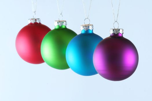 Row of four Christmas ornaments hanging on blue background.