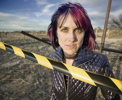 Punk girl outdoors behind a strip of yellow and black caution tape