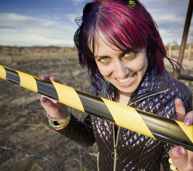 Punk girl outdoors behind a strip of yellow and black caution tape