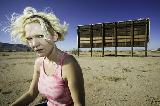 Woman with a sour expression in front of an old billboard waiting in the desert.