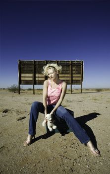 Woman sitting on suitcases in front of an old billboard waiting in the desert.