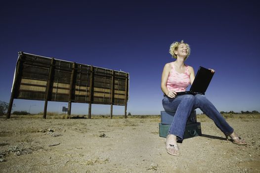 Woman with a laptop computer outside in front of an old bilboard.