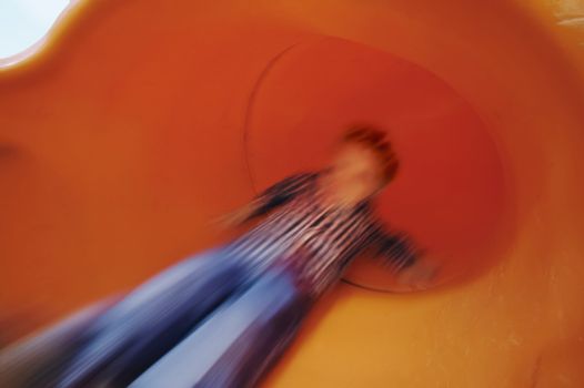 Boy slides down an orange tube slide with motion blur.