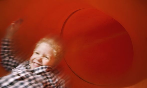 Boy slides down an red tube slide with motion blur.