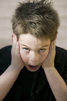 Close up of a surprised young boy with his hands on his face.