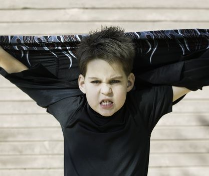 Young boy with his shirt stretched behind his head and a scary look on his face.