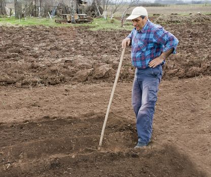 a tired worker is resting holding hie hand on a rake