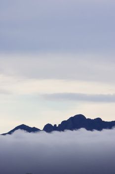 Clouds above and below a mountain ridge.