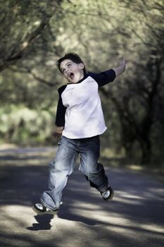 Young boy on a tree-lined path jumps in the air.