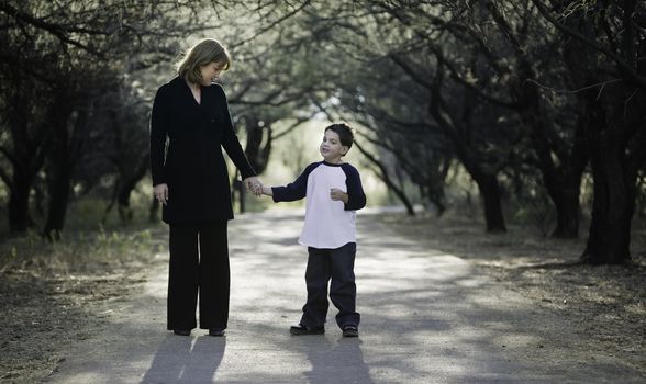 Young boy with his mother on a tree-lined path.