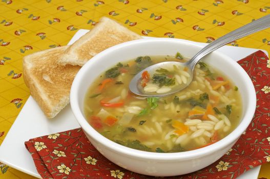 Vegetable soup with pasta served with bread slices on a colorful tablecloth