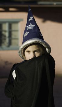 Youn boy with a wizard hiding his face in front of a pink house