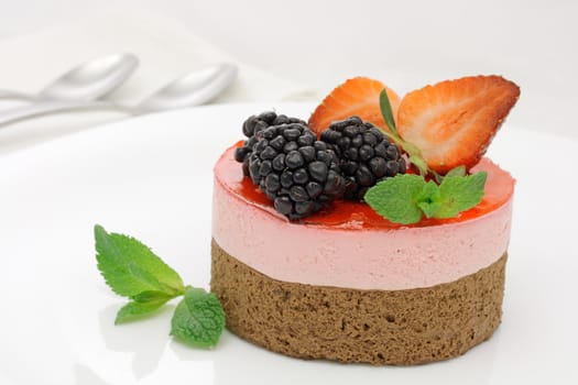 Chocolate and strawberry layer mousse cake, decorated with strawberry slices, mulberries and mint leaves