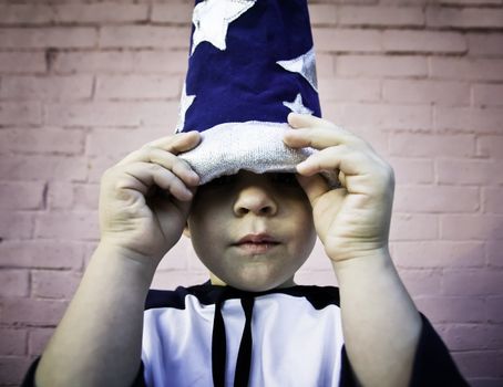 Young boy lifts the brim of a wizard hat and peers out.