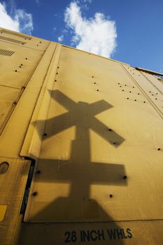 Shadow of a railroad crossing sign cast against the yellow side of a freight train car.