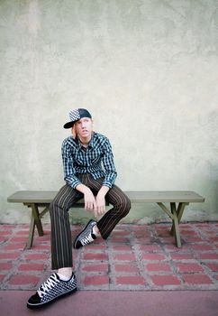 Teenage boy sitting on a green bench in front of a stucco wall